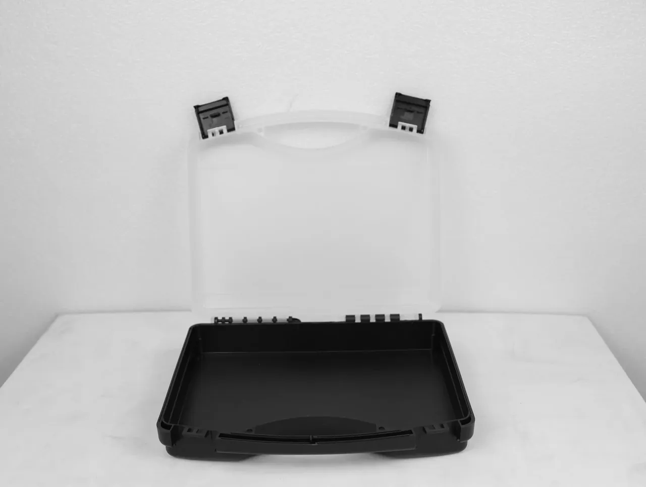 Case Assembly Workstation: a clear case lies open, lid upright behind it, two black latches at the lid corners, black cavity on a marble bench