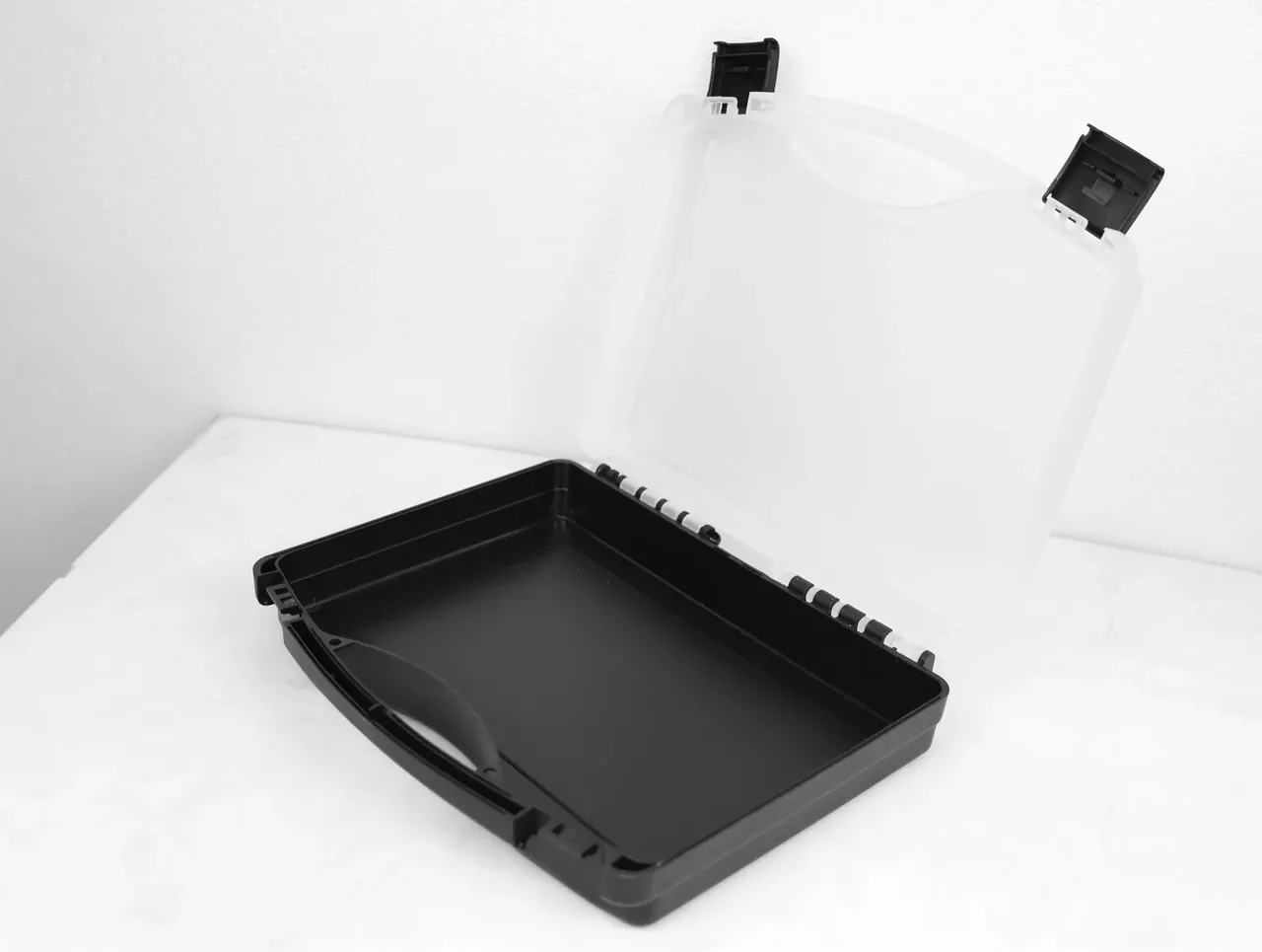 Case Assembly Workstation: black base angled left, frosted lid swung rear right, ribs inside the base, hinge pins in a row, latches up