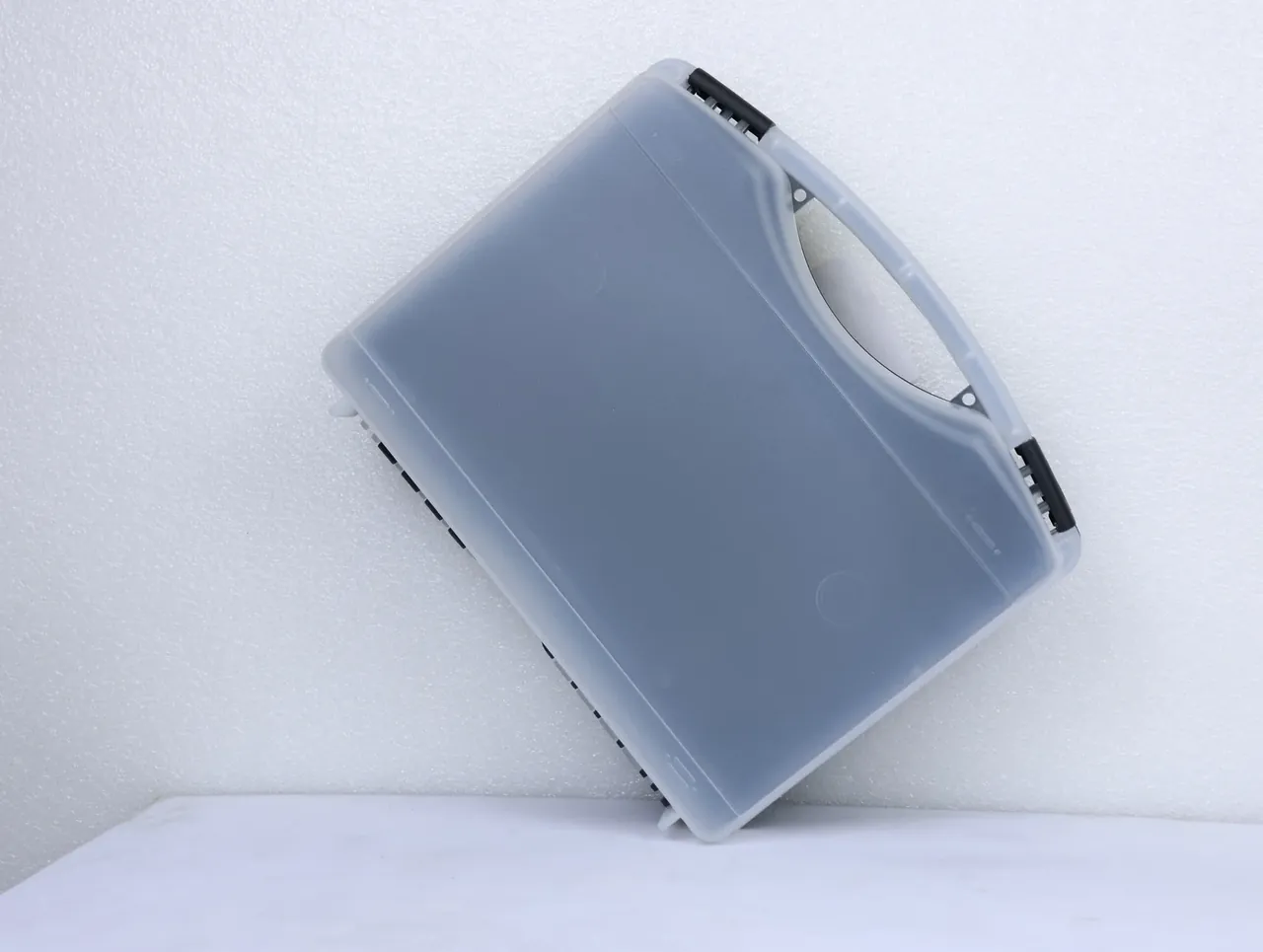 Case Assembly Workstation: a translucent frosted case leans on a white bench, a black hinge block in each upper corner, handle moulded into the lid