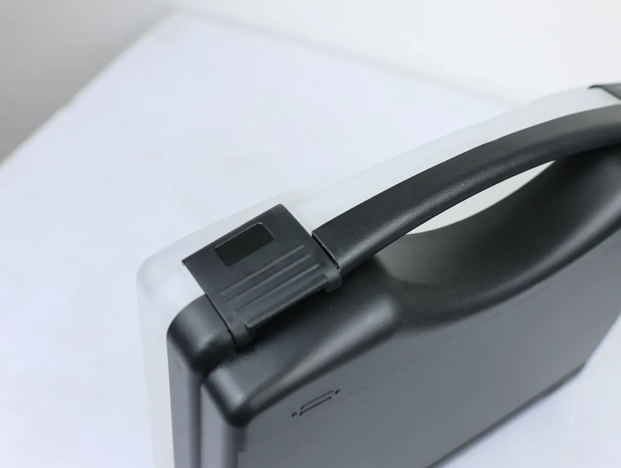 Case Assembly Workstation: close-up of a black case lid, arch handle across the top, a square latch at each end, white bench below