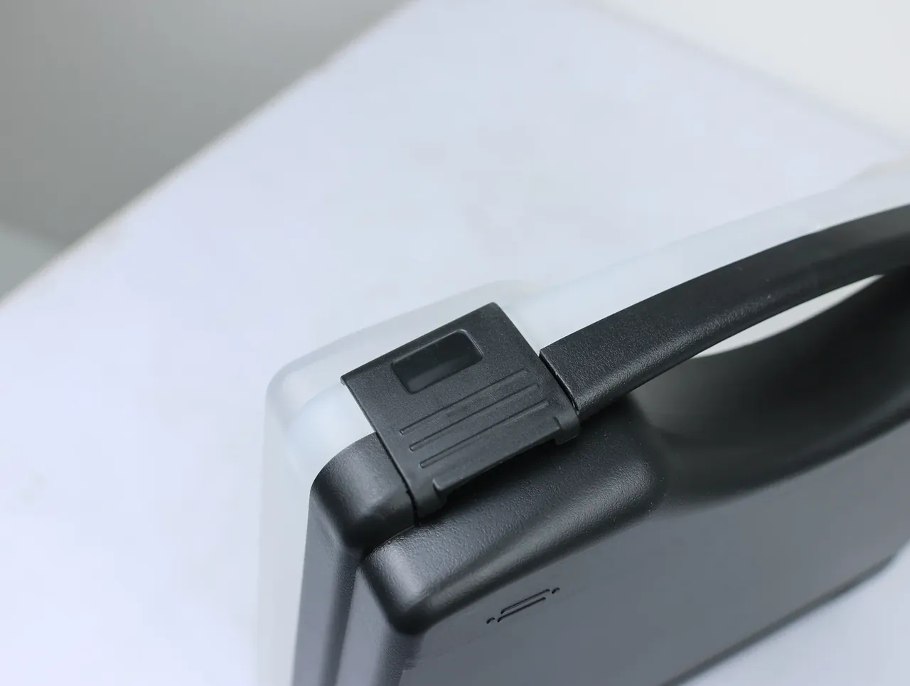 Case Assembly Workstation: one corner of a black lid, a square latch gripping the rim, four raised ribs on its face, handle passing above