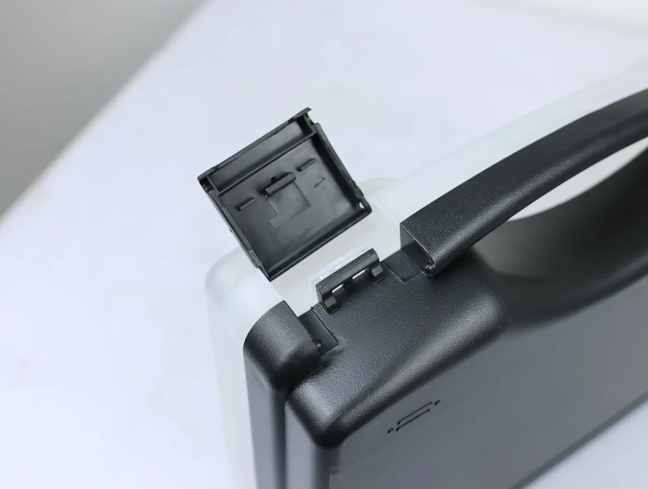 Case Assembly Workstation: latch flipped open, showing a square recess and two stiffening ribs inside, hinge teeth along the lid edge below