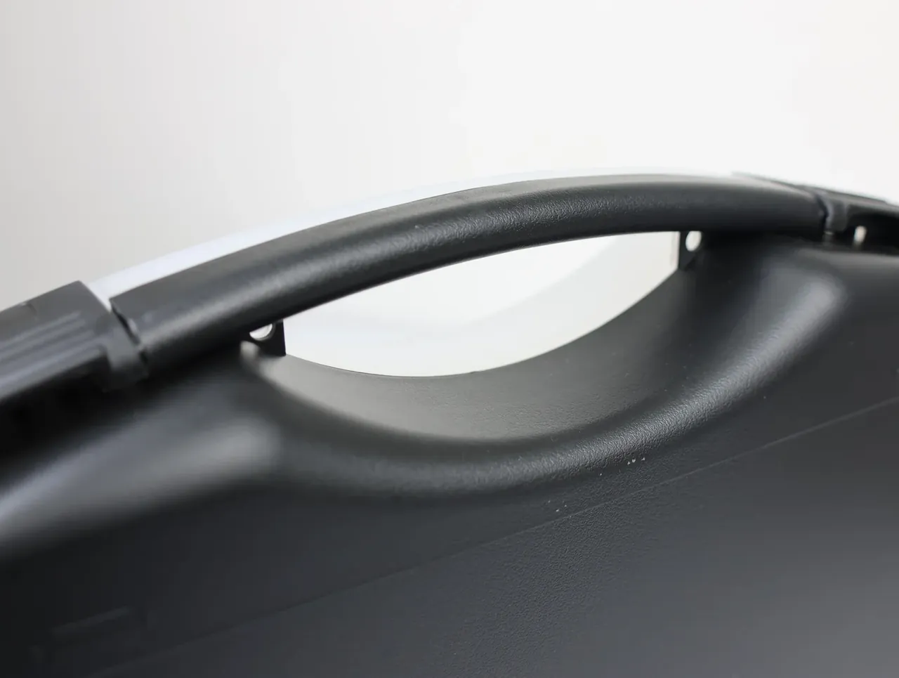 Case Assembly Workstation: front view of the moulded arch handle on a black lid, both ends sunk into the shell, white bench behind