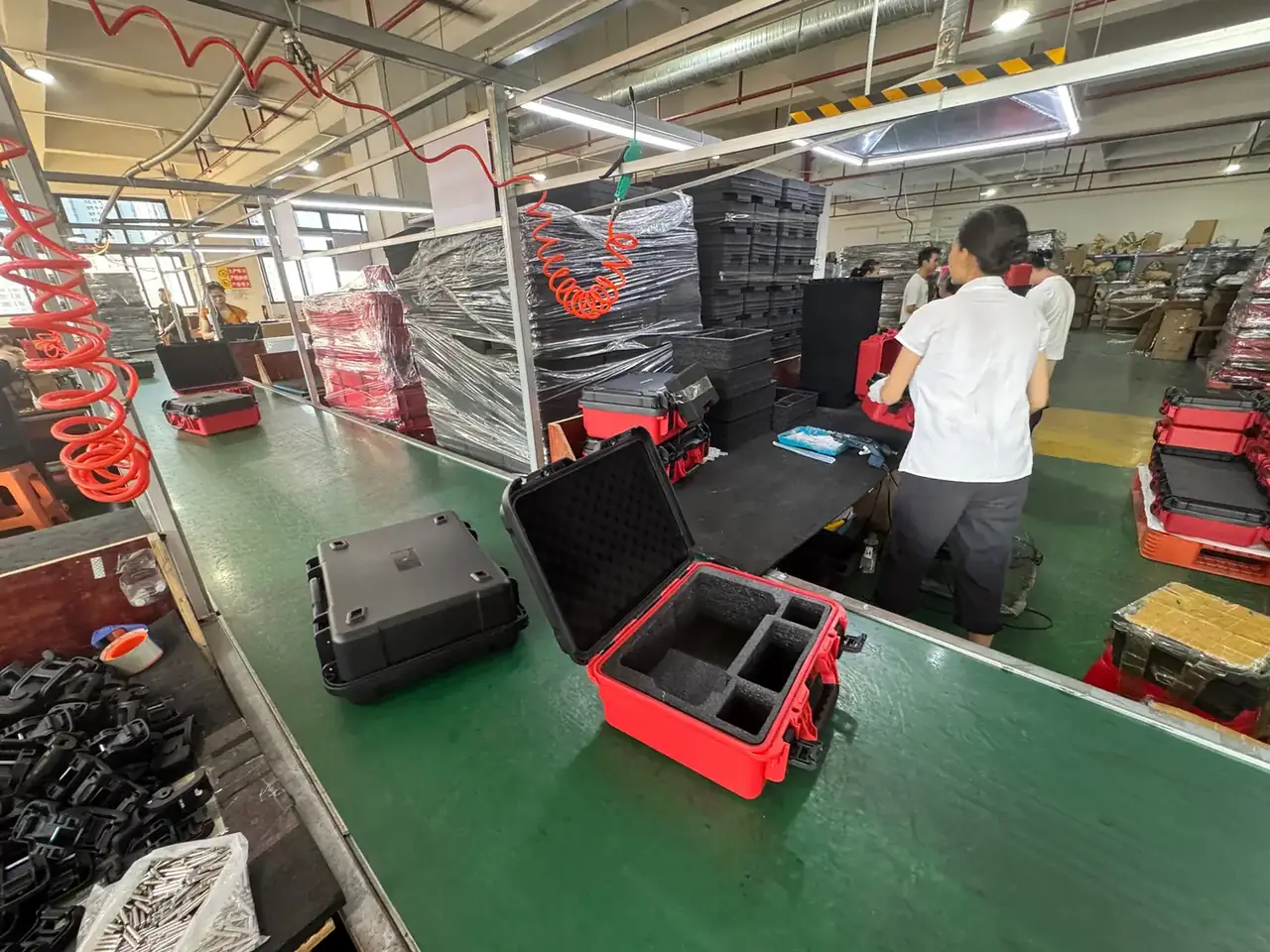 Case Mould: red open case on a green-floor assembly line, black egg-crate foam insert, closed black case in front, red spiral air hoses overhead