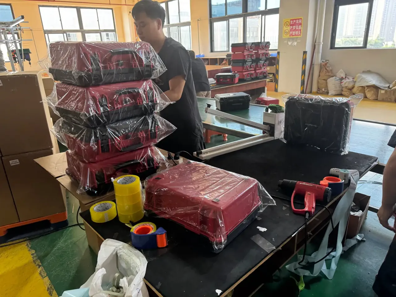 Case Mould: four red tool cases stacked in shrink wrap, a worker beside them, yellow and blue tape plus a red heat gun.