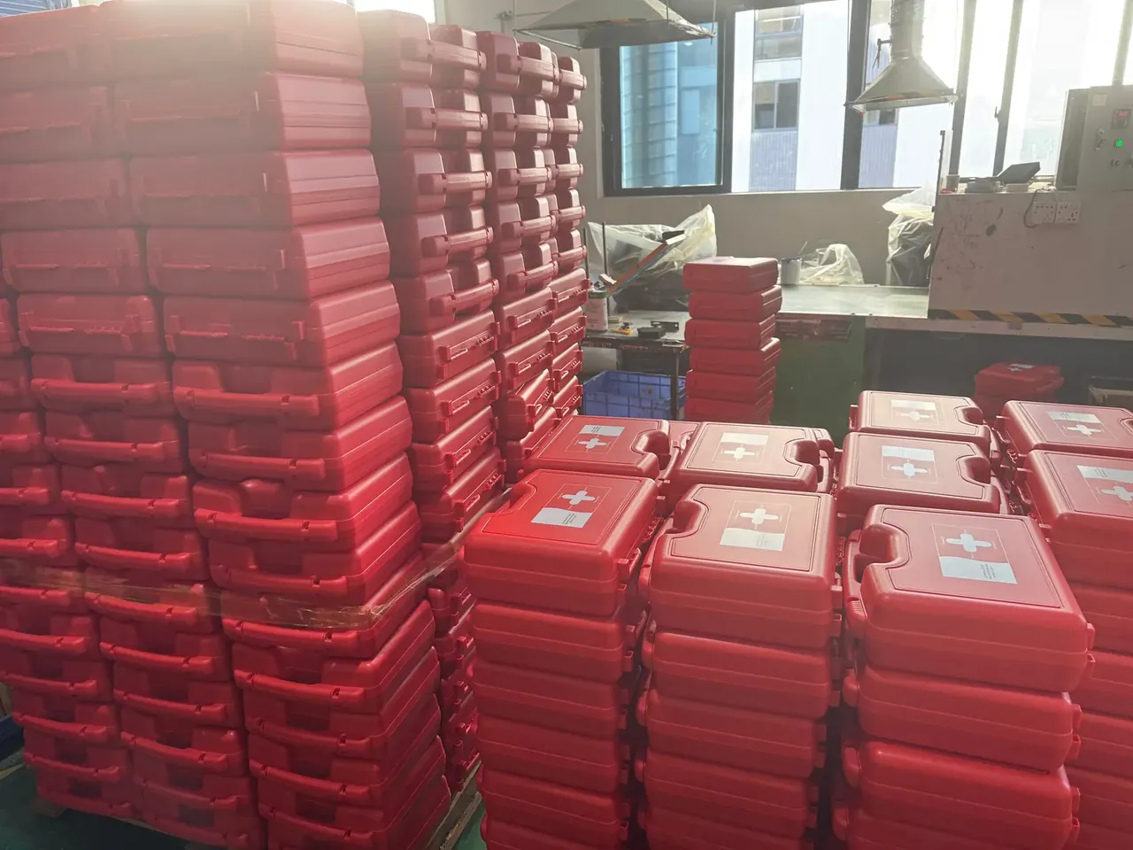 Case Mould: red plastic cases stacked in tall rows on a workshop floor, white cross labels on the lids, windows and a pendant lamp behind.