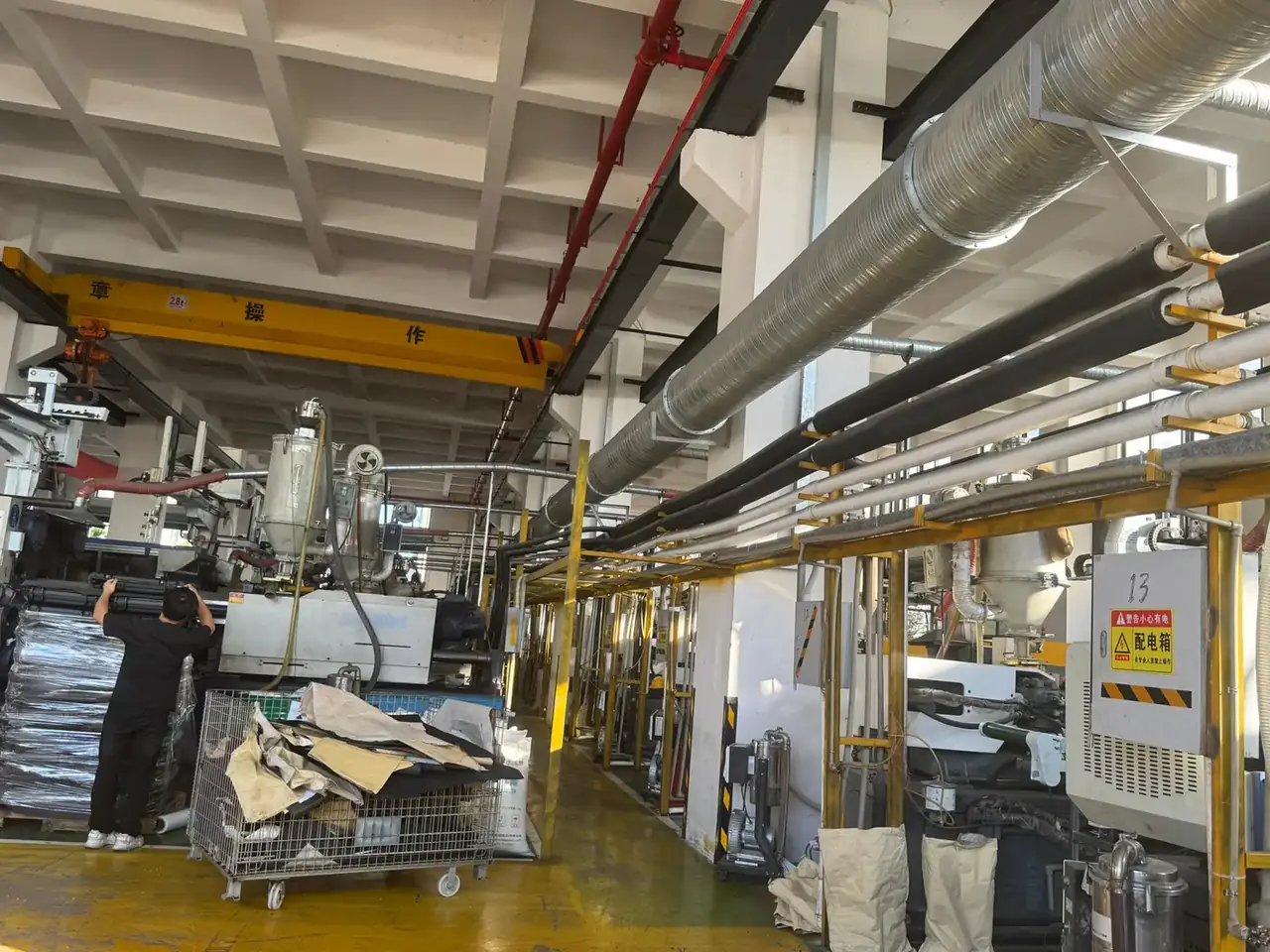 Case Mould: a yellow 28-tonne crane beam spans the moulding shop ceiling, hoppers and ducts along yellow frames, a worker beside a wrapped pallet