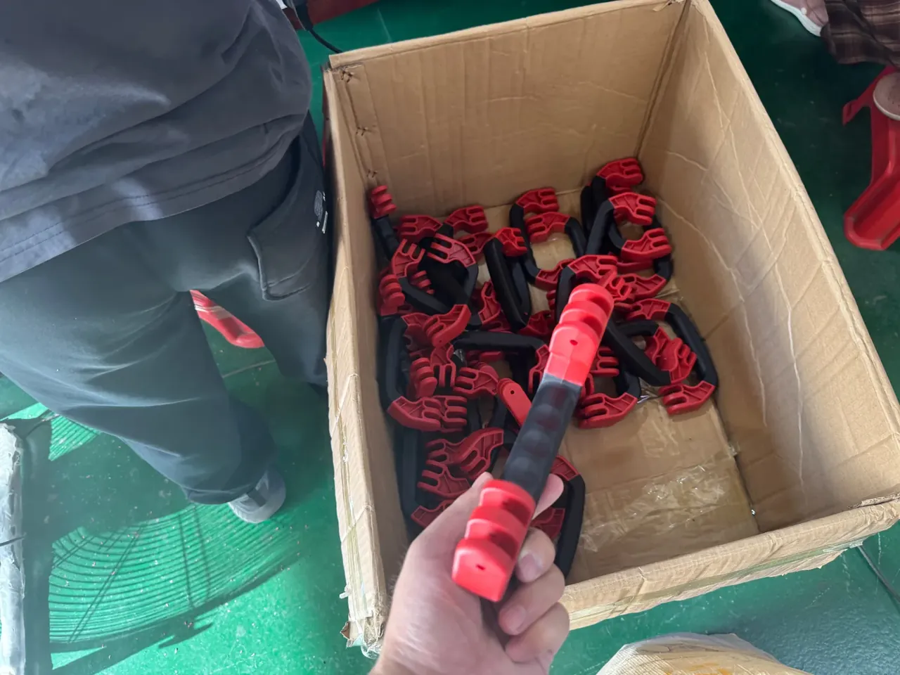 Case Mould: a carton packed with red and black plastic clamps, one clamp lifted by hand above the box