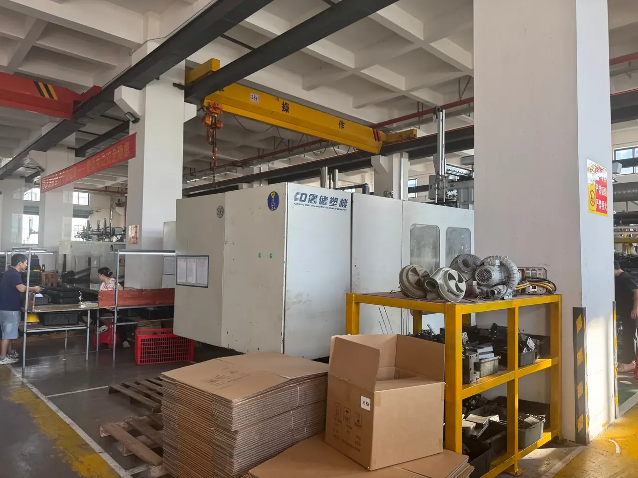 Communication Equipment Case: yellow gantry beam marked 2.8t, a white moulding machine behind, cast blower wheels on a yellow trolley, open carton in front