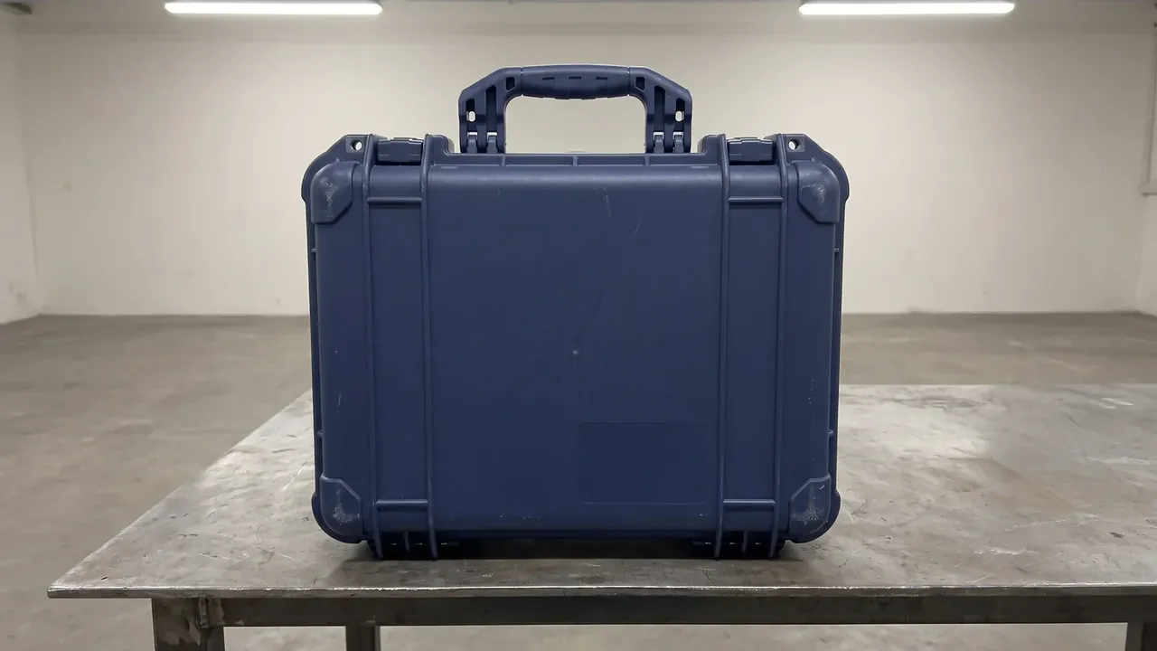 Electronic Equipment Case: navy case closed and standing on a scratched steel bench, moulded top handle, grey corner bumpers, plain white room