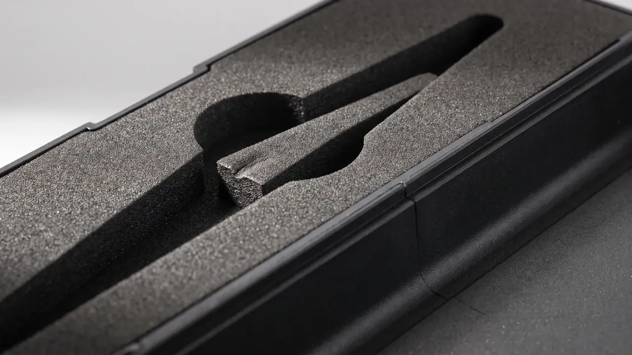 Scene Kit close-up of a black EVA insert with two long cut recesses, fine-grained foam surface, ribbed wall edge and hinge knuckles at left