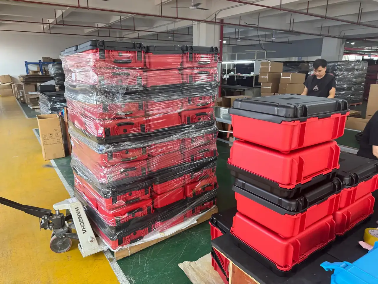 Injection Molded Protective Case: shrink-wrapped red and black cases on a pallet beside a white hand pallet truck, four more stacked on the bench