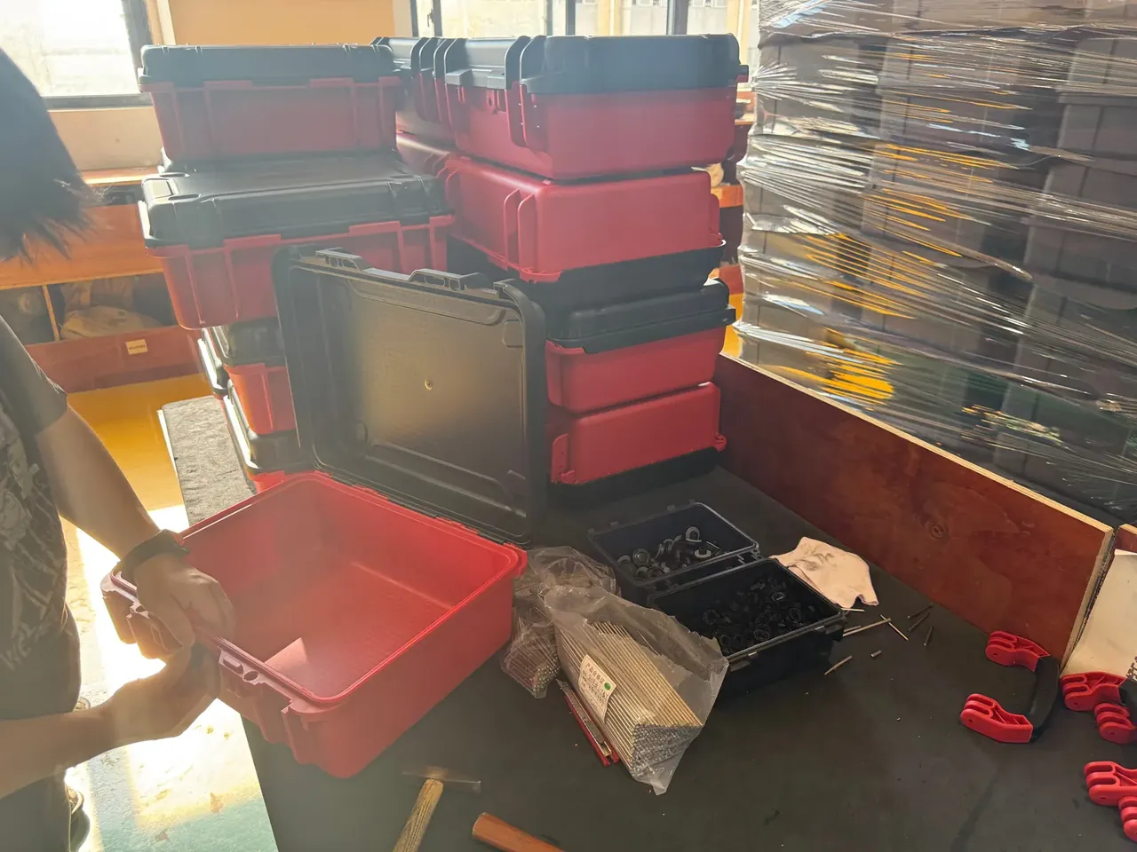 Injection Molded Protective Case: an open red case with an empty bare interior, lid upright, two trays of black fasteners beside a claw hammer