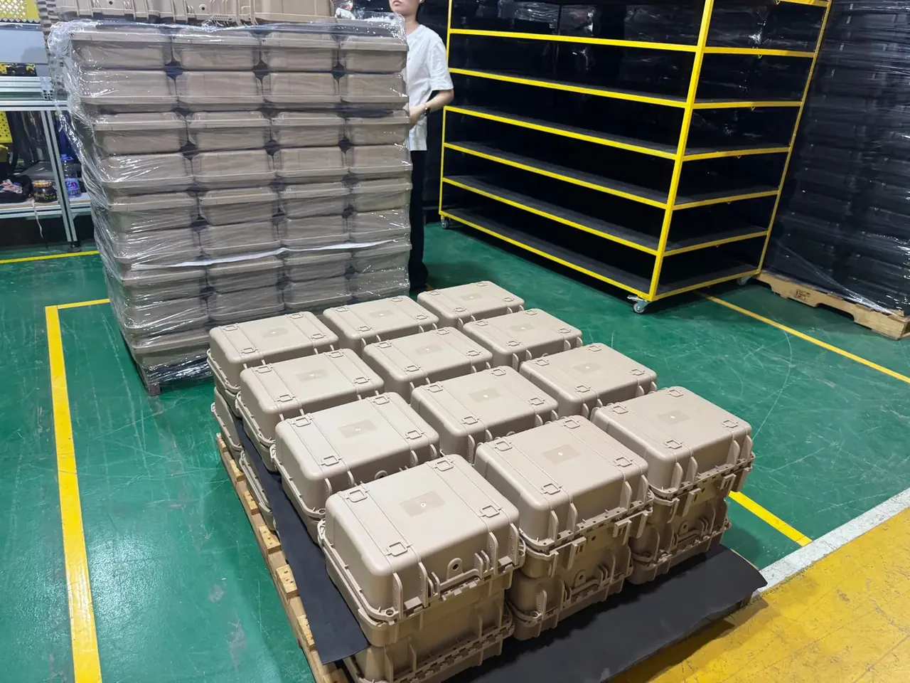 Injection Molded Protective Case: a wall-high stack of sand-coloured cases in clear film, a dozen more on a pallet, a five-tier yellow rack beside them
