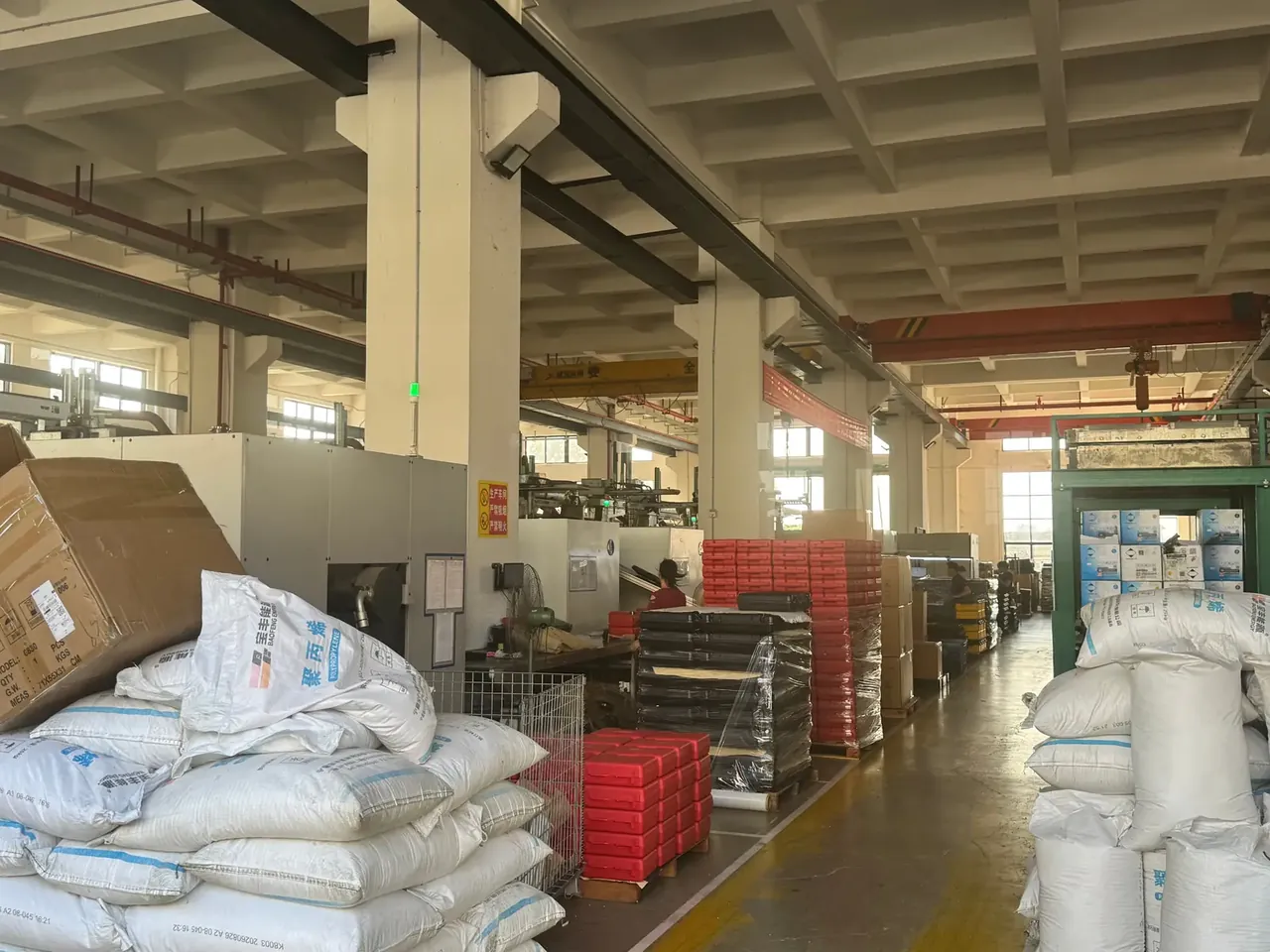 Injection Molded Protective Case: white polypropylene resin sacks in the foreground, moulding machines down the gangway, red and black crate stacks beside them