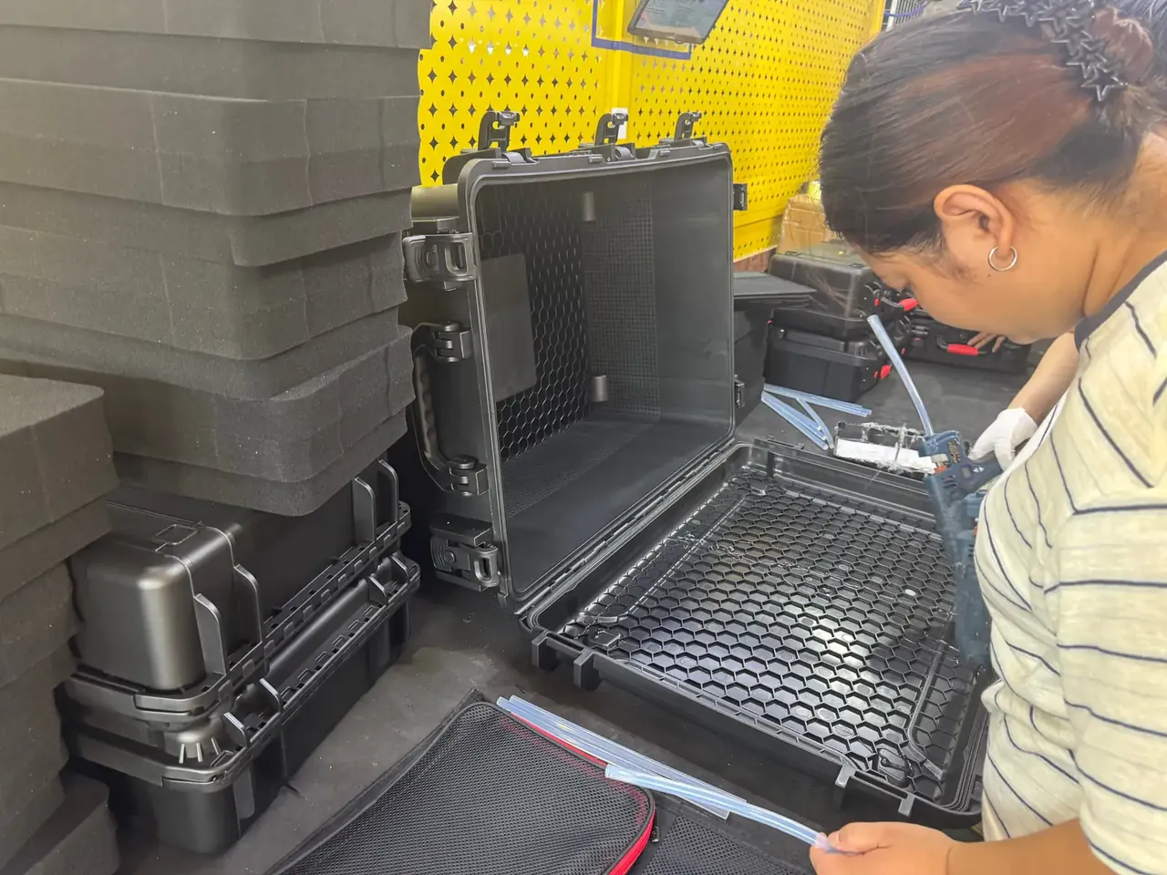 Injection Molded Protective Case: open black case showing honeycomb ribs inside the lid, stacked black foam at left, worker in a striped shirt beside it