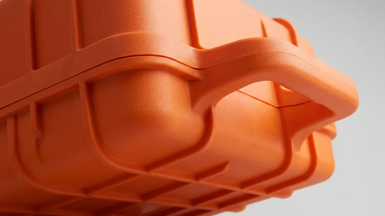 Custom plastic case: orange flank close-up, crossed ribs in a grid, moulded handle across the middle, rounded corners, pale backdrop