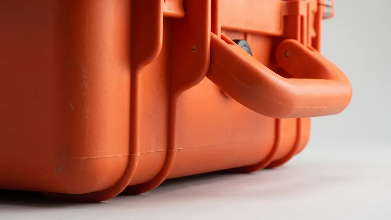 Custom tool box in orange seen close on the side, two folding handles against the wall, vertical corner ribs and feet below
