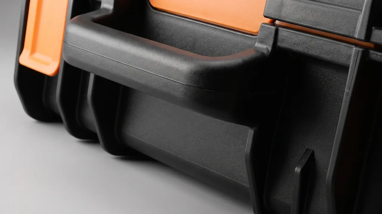 Portable travel case: black textured side wall, a moulded horizontal handle sunk into a recess, one orange latch at the left edge