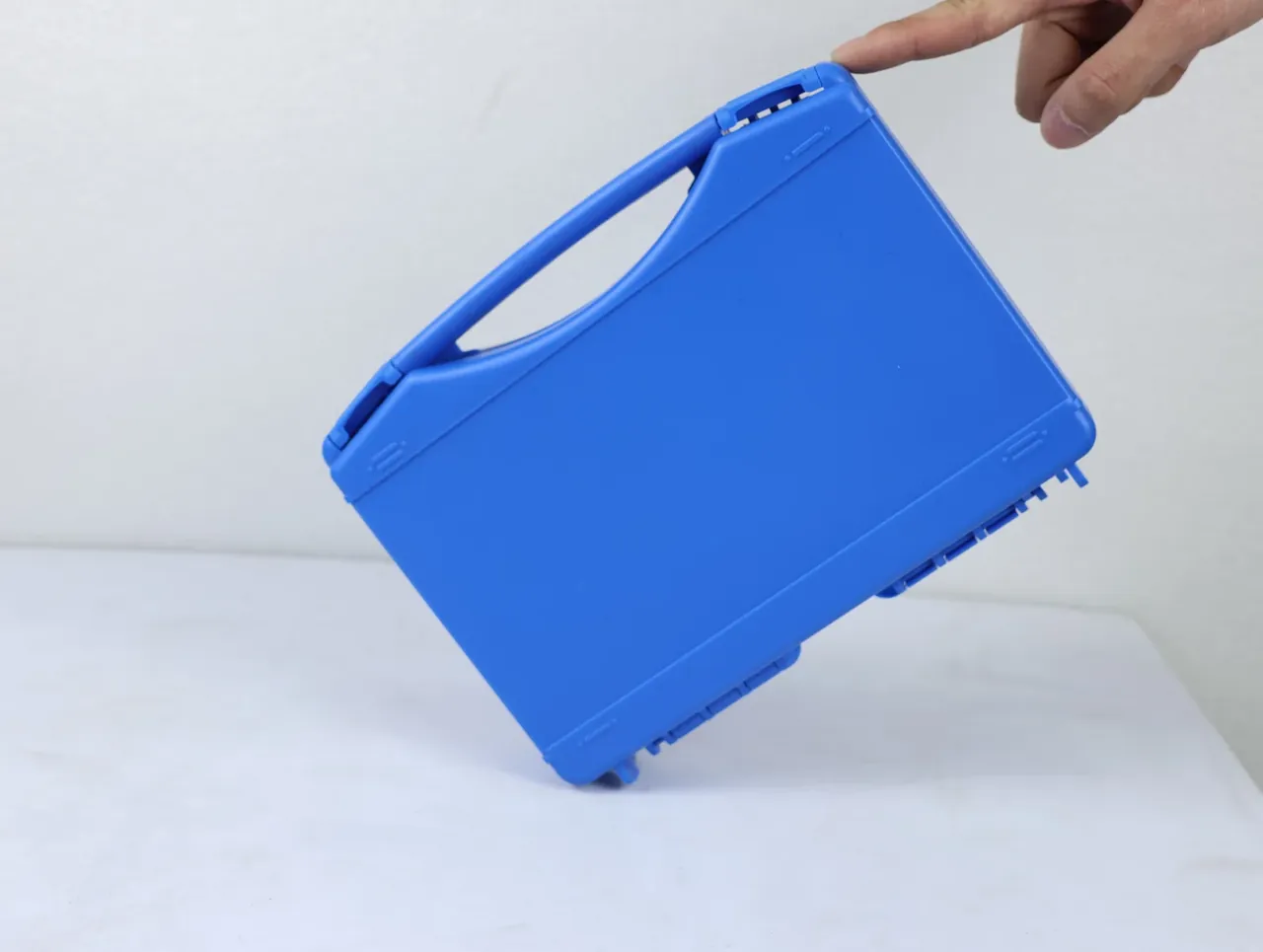 Large Protective Case: the same blue case on a white table, long handle and lid rim up, fingers at the top corner, rounded edges