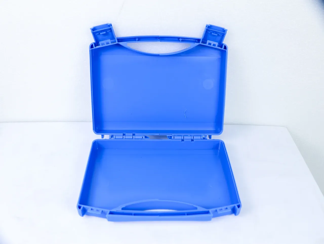 Large Protective Case: a blue case lying open and empty, curved handle cutout in the lid, a hinge row between halves, white foam board behind
