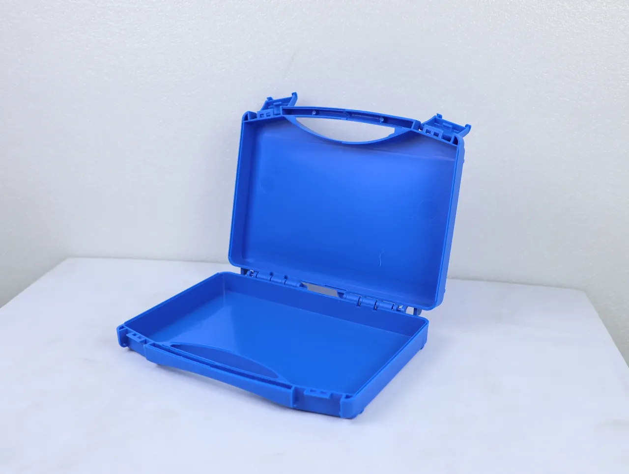 Large Protective Case: a blue case at an angle on a white stone tabletop, lid raised, empty base tray, hinge row, rounded corners
