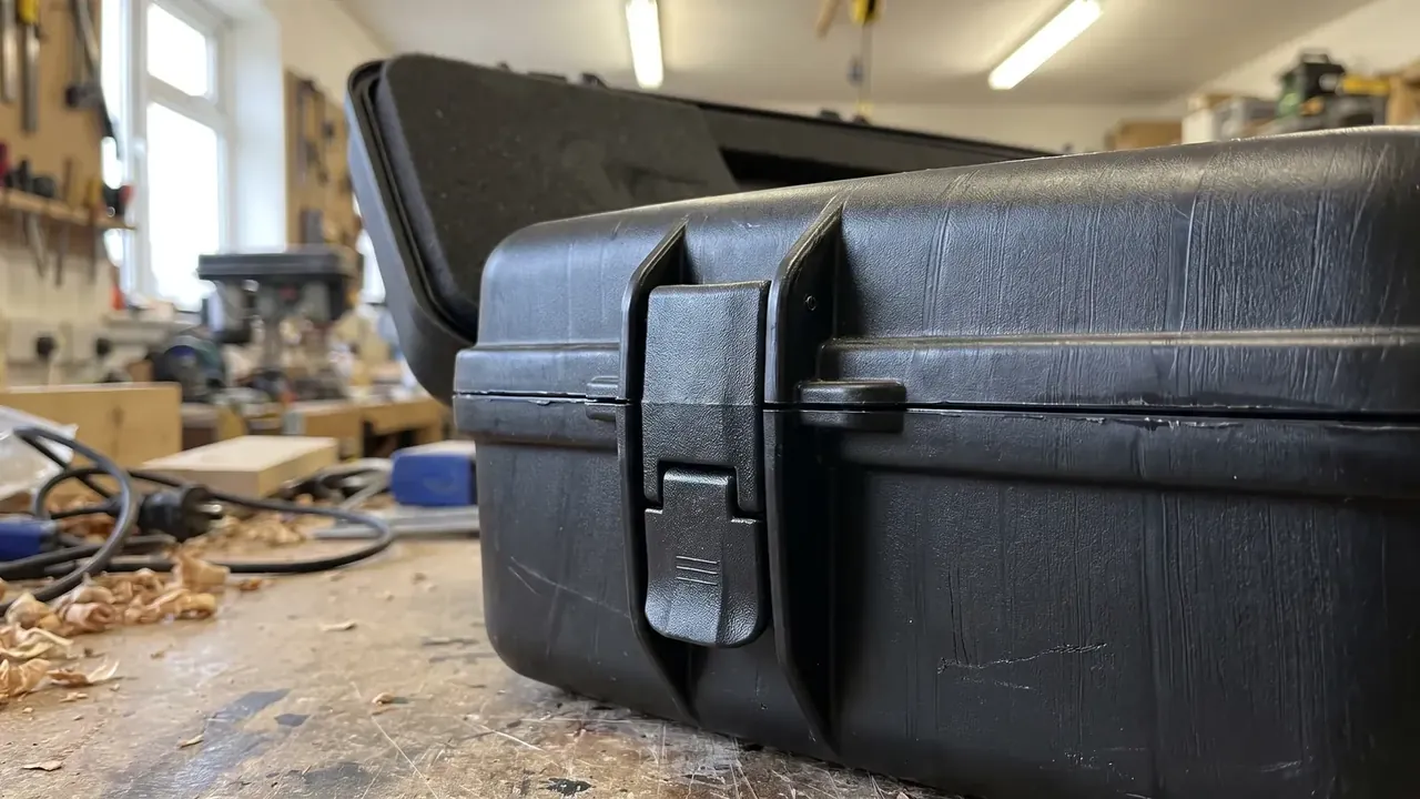 Measuring Instrument Case: black case on a workbench, lid tilted back, one latch closed, shavings and cables on the bench