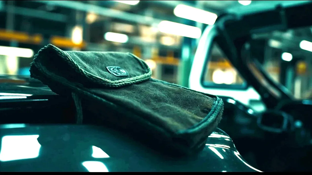 A tool pouch resting on a car wing during an assembly line task, no faces