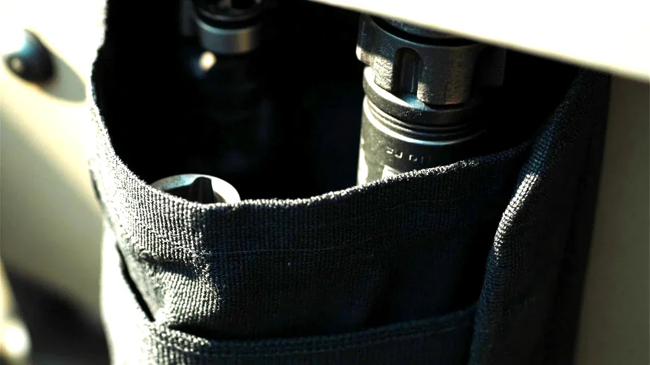 Close-up of a tool pouch outer pocket holding a ratchet and two sockets, elastic keepers visible