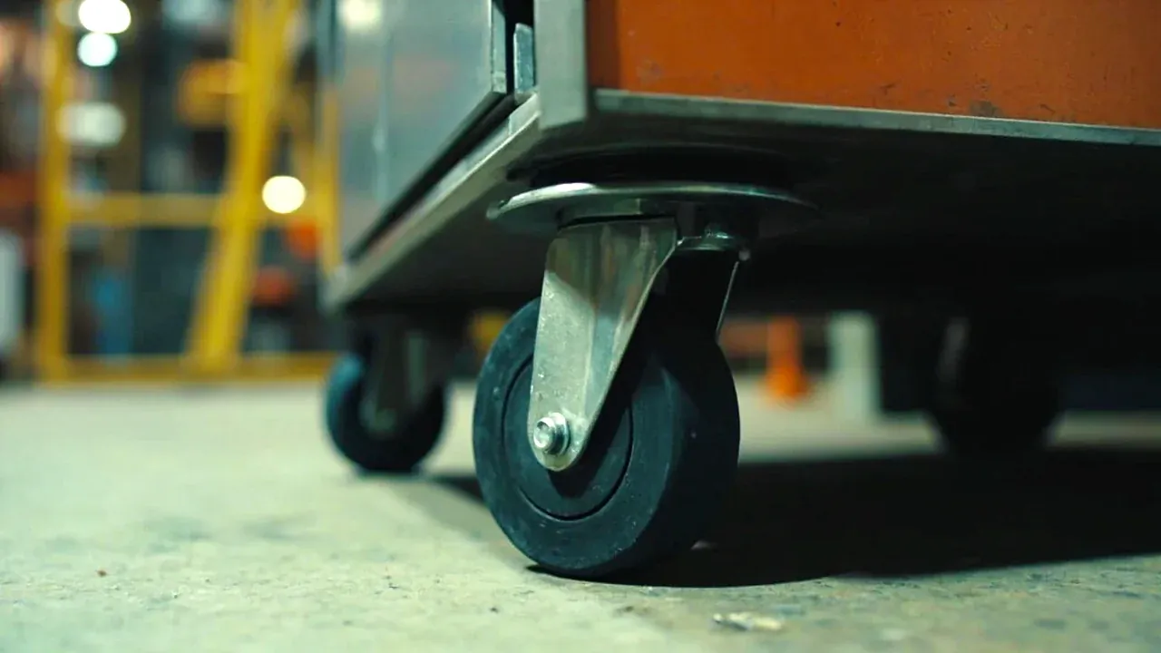Close-up of a large castor and a smaller swivel castor under a mobile tool cabinet, one brake engaged