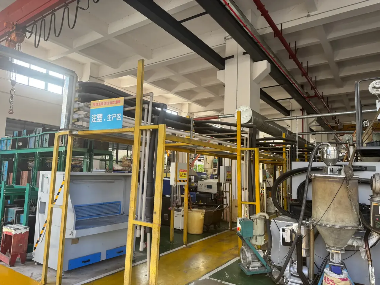 Pistol Case: yellow steel frames enclosing a moulding area, a blue sign overhead, dryer hopper and barrel at right, yellow walkway between columns