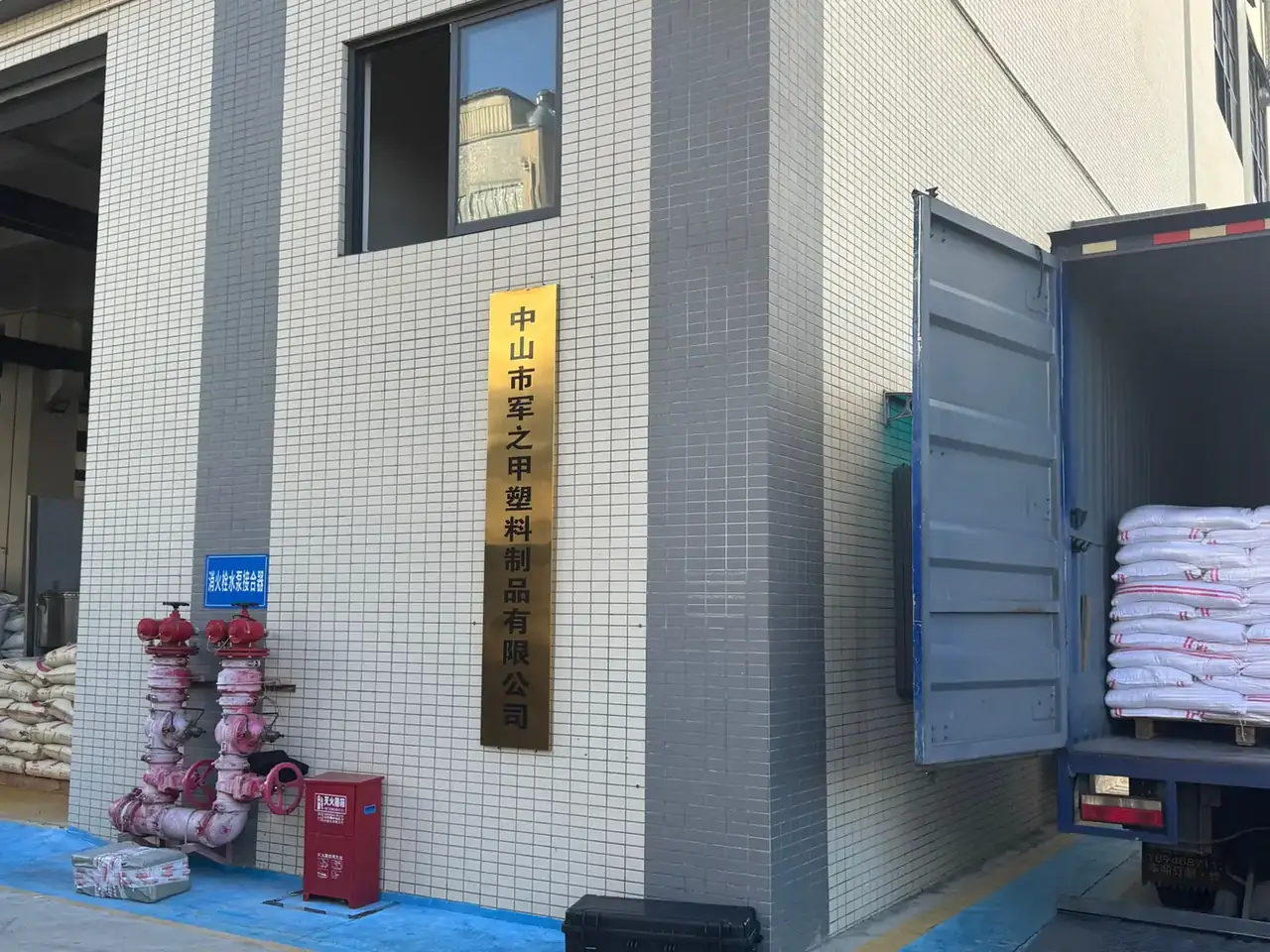 Plastic Tool Box, Portable: a tiled factory wall with a gold vertical sign, red fire valves below, and a lorry loaded with white sacks