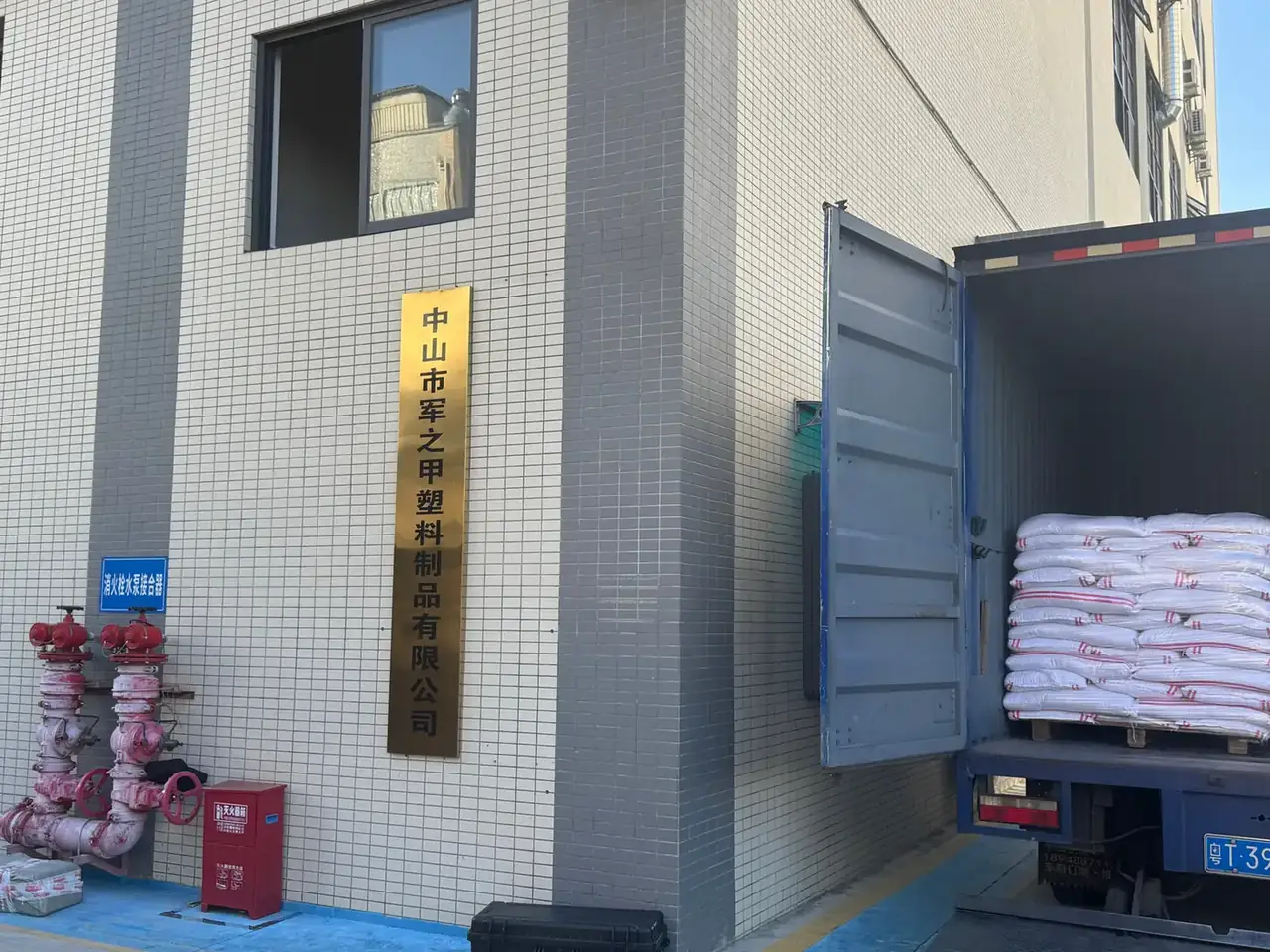 Plastic Tool Box, Portable: a tiled factory wall with a gold signboard, red fire hydrant valves and an open box truck loaded with white sacks