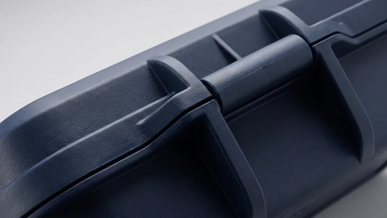 Tool box lid handle close-up, navy plastic pivot pin through two moulded lugs, parting line and matte texture under side light