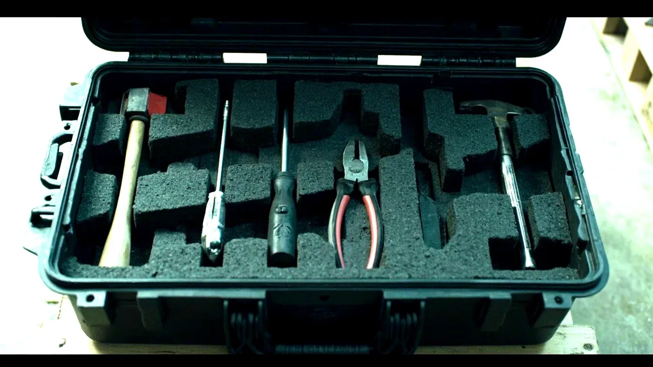 Top-down view of an open black tool box, foam compartments holding screwdrivers, pliers and a hammer