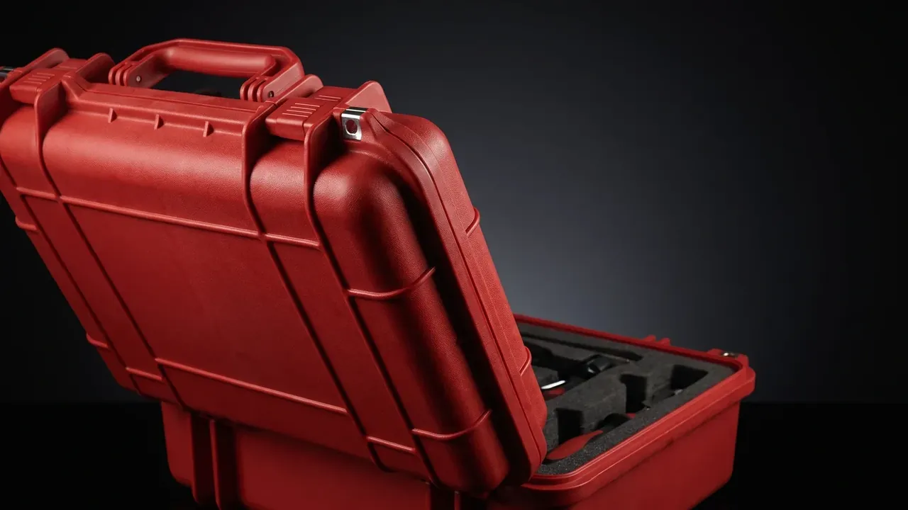 Tool Bag: red hard case at an angle, lid half open showing black foam with cut-outs, one-piece top handle, metal latch and corner ribs