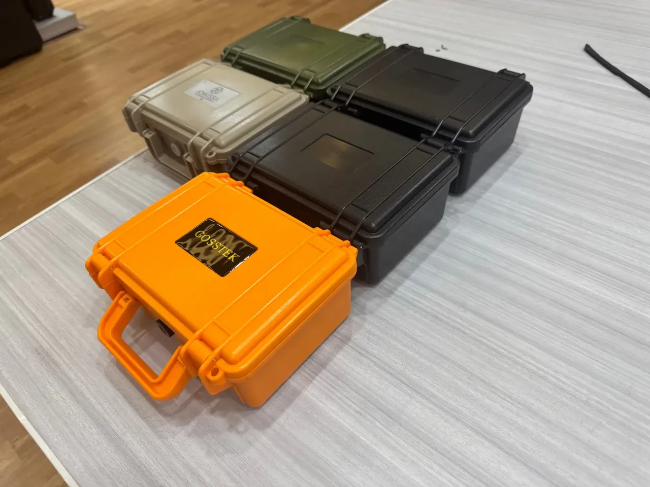 Tool Bag: five hard cases in different colours on a grey woven mat, an orange one with a black label, wood floor behind