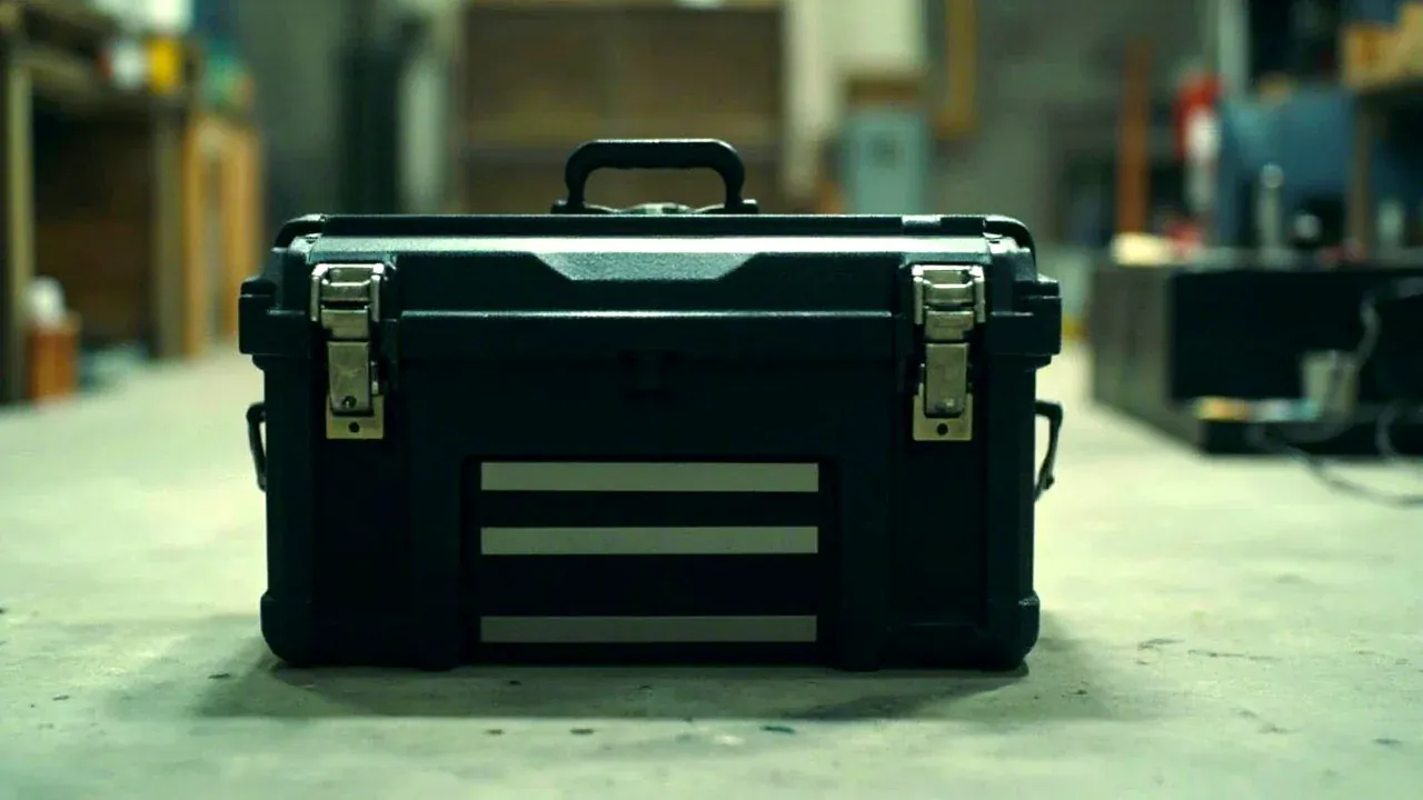 A closed tool kit chest with two draw latches and a carry handle on a workshop floor