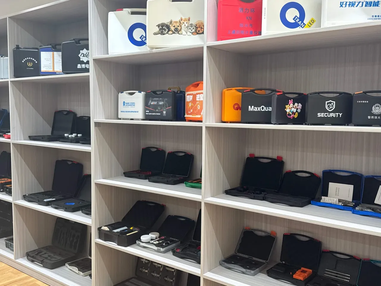 Tool Roll: white wood shelving in five tiers holding black, orange and beige hard cases, several open below showing dark inserts
