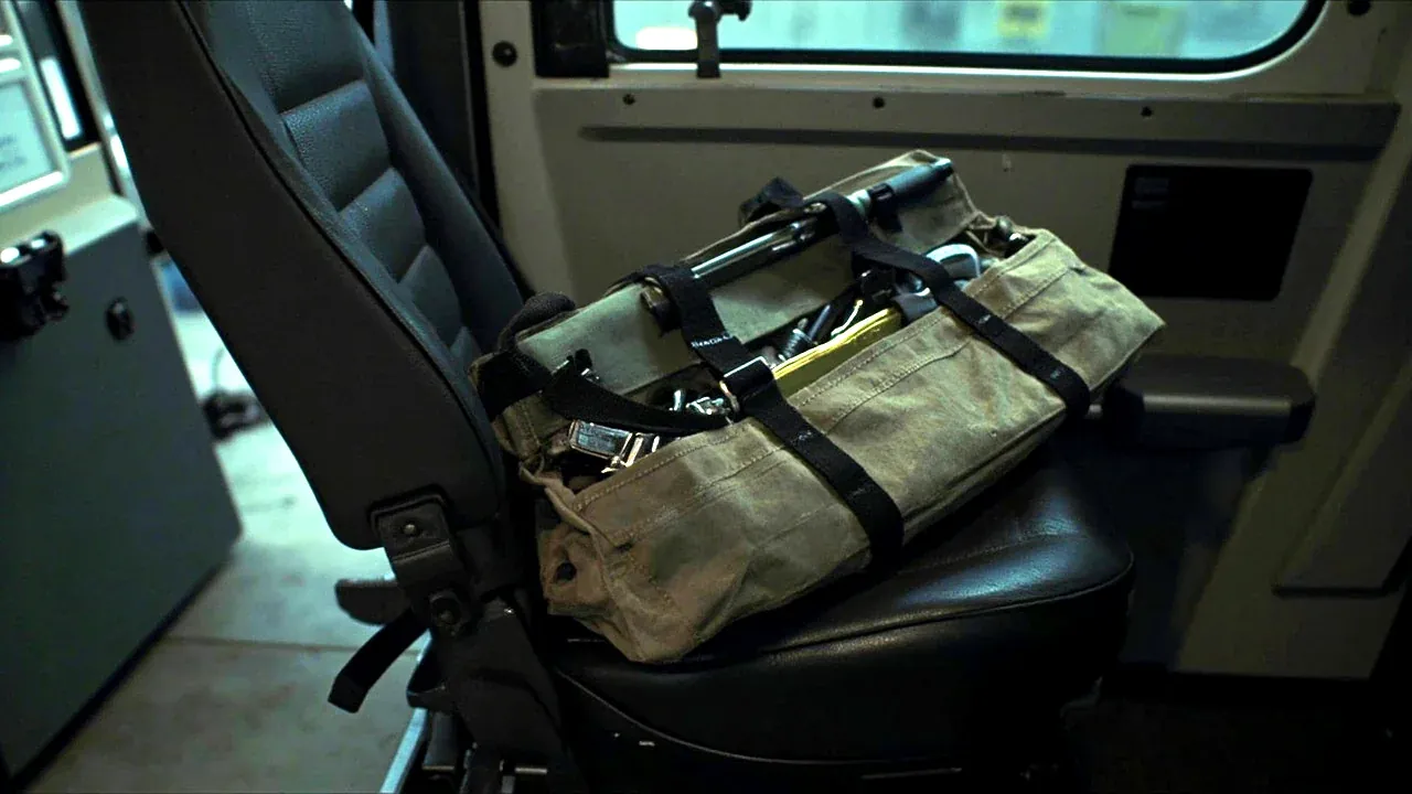 A tool satchel on the seat of a service vehicle, secured by a strap, tools inside