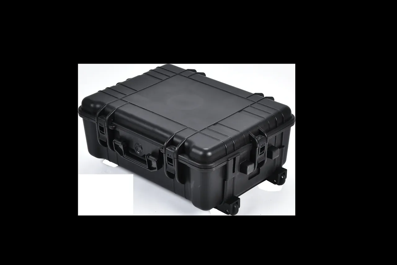 Black case lying flat seen from above, two latches and a round badge on the front, a small wheel at the lower right